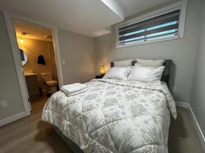 a bedroom with a bed with a white comforter and a window at Eli's Place in Calgary