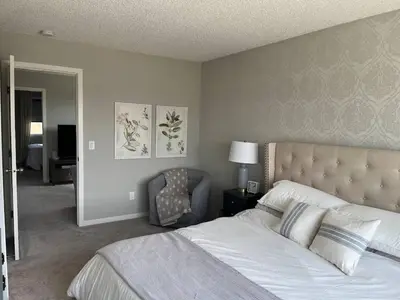a bedroom with a large bed and a chair at Le Reve Show Home 3BD, AC, sleep 9 , Beaumont in Nisku