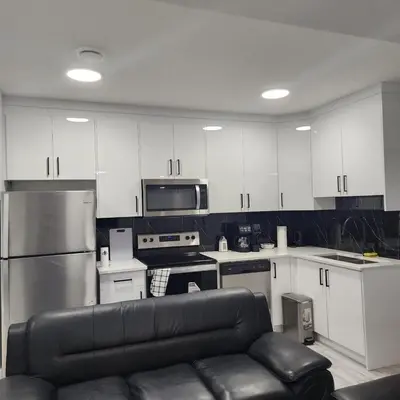 a kitchen with white cabinets and a black leather couch at Spacious 2 Bedroom Suite in Edmonton, Canada in Edmonton
