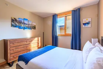 a bedroom with a bed and a window with blue curtains at Boardwalk Bliss - Top Floor Downtown Condo in Canmore