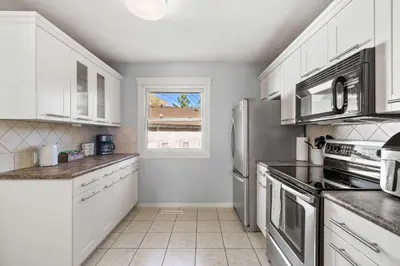a kitchen with white cabinets and stainless steel appliances at Nineteen55 4BR Parkside Home in Central Red Deer in Red Deer