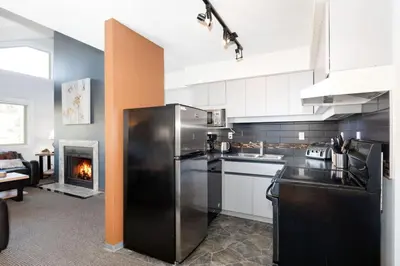 a kitchen with a stainless steel refrigerator and a fireplace at Whistler Corner Loft Next to lift with Amazing views! in Whistler