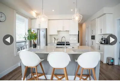 a kitchen with three white chairs and a kitchen island at Ventura in Downtown in Abbotsford