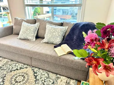 a couch with two books and a vase of flowers at Private Entire Guest Suite, 1 min to bus stops to Downtown and major attractions in Vancouver