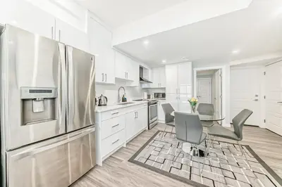 a white kitchen with a table and a refrigerator at 2 Beds, 1 bath Walkout Basement in Calgary