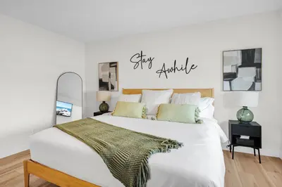 a bedroom with a white bed with a stay awhile sign on the wall at New Luxury Sleeps 7 AC Double Garage in Edmonton