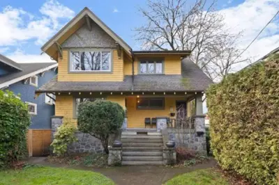 a yellow house with a staircase in front of it at Charming 2 bedroom Duplex steps from Jericho Beach in Vancouver