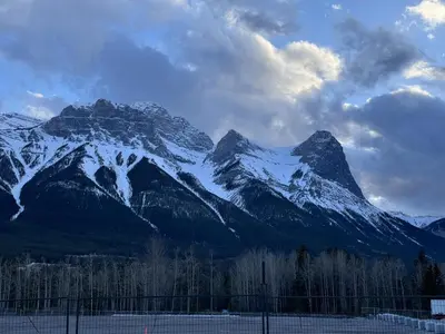 a snow covered mountain in front of a fence at Cozy Canmore resort with mt view hot tub and pool in Canmore