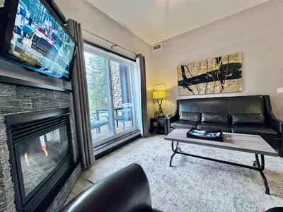 a living room with a black couch and a fireplace at Cozy Canmore resort with mt view hot tub and pool in Canmore