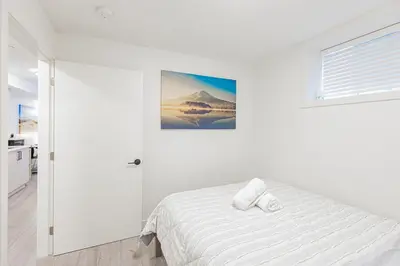 a white bedroom with a bed and a picture on the wall at Dumfries Guest Room in Vancouver in Vancouver