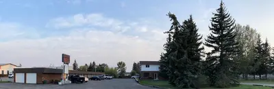 a building with a parking lot next to some trees at Rest Easy Motel in Three Hills