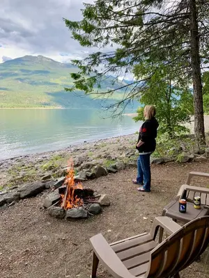 a woman standing next to a campfire next to a lake at Wing Creek Resort in Kaslo