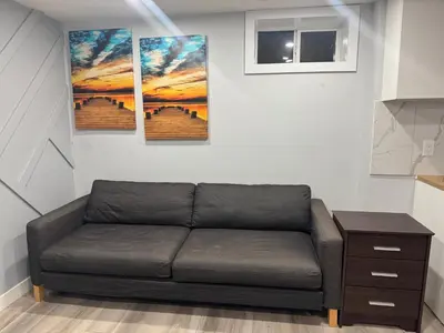 a couch in a room with three paintings on the wall at Spacious 2 bedroom 3 beds lower unit with separate entrance and parking space Near Downtown, Calgary Zoo, Costco and many more in Calgary