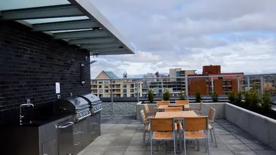 a patio with a grill and tables and chairs on a balcony at Sunset Place-Deluxe One Bedroom Condo in the Escher Building, Sunset Views and Beyond in Victoria