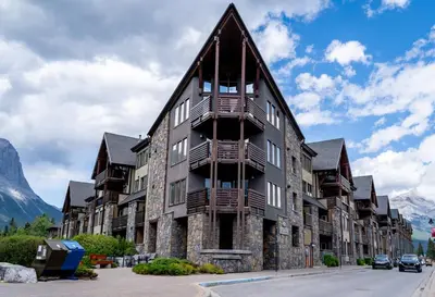 an apartment building in the mountains with mountains in the background at Creekside 2-Bedroom Condo in Canmore