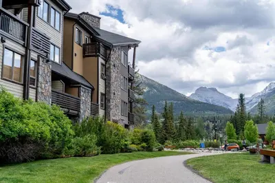 a building with a path in front of a mountain at Creekside 2-Bedroom Condo in Canmore