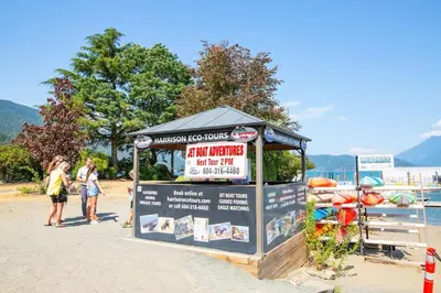 a kiosk on a beach with people standing around it at The Riverbend Modern Studio at Harrison Lake in Harrison Hot Springs