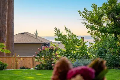 a yard with a house with a fence and flowers at New 2BR Suite With Great Ocean View in West Vancouver in West Vancouver