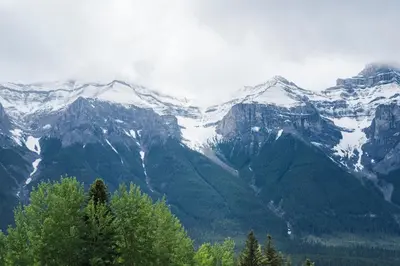 a snow covered mountain range with trees in the foreground at Rocky Mountain Gem - One Level 750 sq ft - Hot Tub - Quiet Condo - Self Check-In - Free Parking - BBQ Fire Pit Area in Canmore