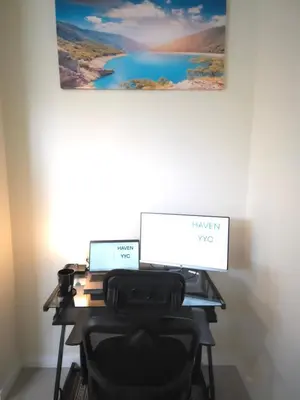 an office desk with two computers and a painting on the wall at Haven YYC Guest Suite in Northwest Calgary in Calgary