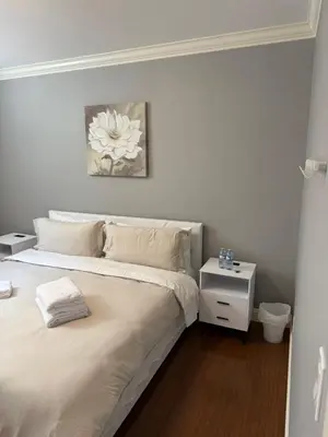 a white bedroom with a bed and a night stand at Peaceful & Cozy Home with 3 rooms, SHARED Bathrooms and SHARED Common Space in Vancouver
