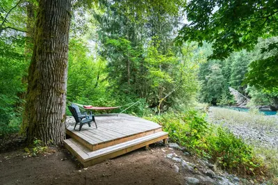 a hammock sitting on a wooden deck next to a tree at Riverwood Retreat-hot tub and cedar sauna on the river in Squamish