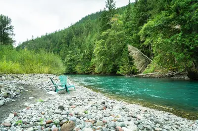 a bench sitting on the shore of a river at Riverwood Retreat-hot tub and cedar sauna on the river in Squamish