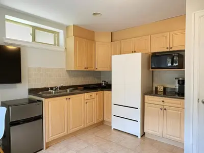 a kitchen with wooden cabinets and a white refrigerator at Bright 1-Bedroom Garden Suite, Sleeps 4, Near Downtown & YVR in Vancouver