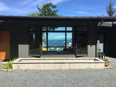 a black house with a view of the ocean at Cokely Cove Guesthouse - Oceanside Villa in Denman Island