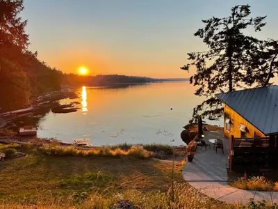 a house on the shore of a lake at sunset at Cokely Cove Guesthouse - Oceanside Villa in Denman Island
