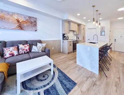 a living room with a couch and a kitchen at Family Modern 1BR and Den Condo - Apartment with City View, Downtown, Balcony, Free Parking & In-Suite Laundry! in Calgary
