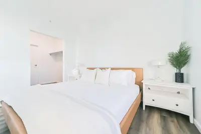 a white bedroom with a large white bed and a nightstand at City View 2 King Suites Floor-to-Ceiling Views in Calgary