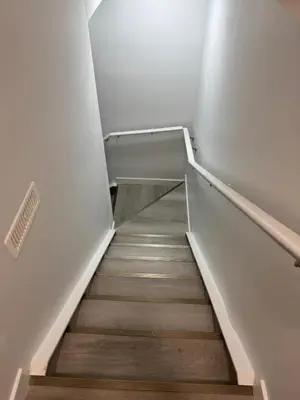 a staircase in a building with wooden floors and white walls at Cozy Inn new basemt wt sep entrance contains 1 bdrm and den for up to 4 guests in Airdrie