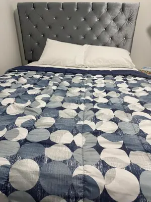 a bed with a blue and white comforter on it at Cozy Inn new basemt wt sep entrance contains 1 bdrm and den for up to 4 guests in Airdrie
