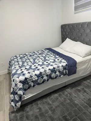 a bed with a blue and white quilt on it at Cozy Inn new basemt wt sep entrance contains 1 bdrm and den for up to 4 guests in Airdrie