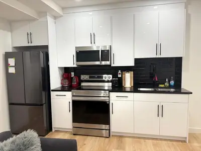 a kitchen with white cabinets and a black refrigerator at Cozy 2-Bedroom Basement Suite Just Minutes from the Airport in Calgary
