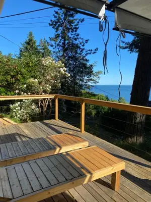 a wooden bench on a deck with the ocean in the background at Cedar House Ocean View & Access in Roberts Creek