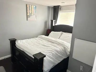 a bedroom with a bed with white sheets and a window at ComfyComfort in Calgary