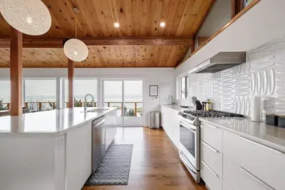 a kitchen with white cabinets and a wooden ceiling at Ocean's Embrace Suite in Nanaimo