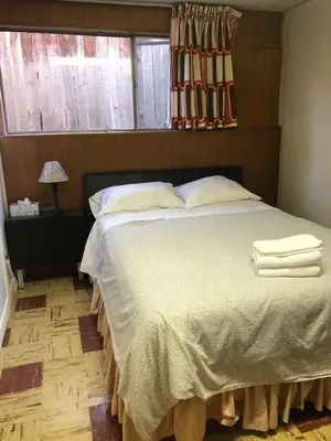 a bedroom with a bed with white sheets and pillows at Comfort cottage guest home near subway station, bus and downtown in Vancouver