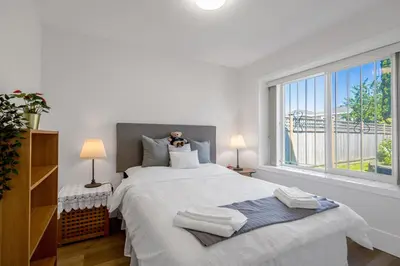 a bedroom with a large bed with two lamps and a window at 2 Bds suite beautiful Yard near PNE in Vancouver