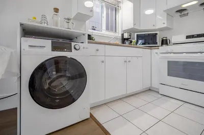 a white kitchen with a washing machine at 2 Bds suite beautiful Yard near PNE in Vancouver