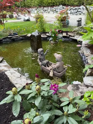 two statues of two children in a boat in a pond at Charming Lakefront 100yr old Railway Cottage in Youbou