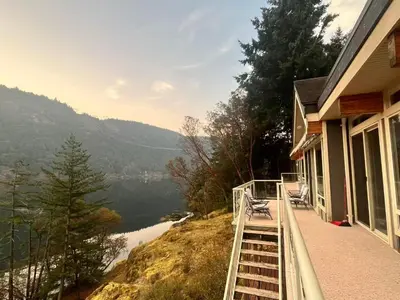 a house with a balcony with a view of a lake at Malahat Fairyland Cottage in Malahat