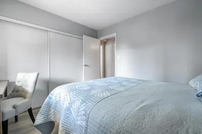a white bedroom with a bed and a chair at YYC HiddenGem in Calgary