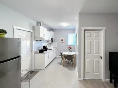 a kitchen with white cabinets and a table and a door at Vancouver Burnaby Villa 36 in Burnaby