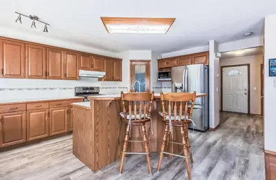 a kitchen with wooden cabinets and two bar stools at Master Bedroom with attached bathroom in Airdrie