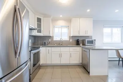 a kitchen with white cabinets and a stainless steel refrigerator at Soothing Minimalist Escape - Suite with Balcony & Fireplace in Vancouver