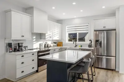 a kitchen with white cabinets and a large white island at King Bed, AC, Fenced Yard, Family Friendly, 5 min South Health Campus in Calgary