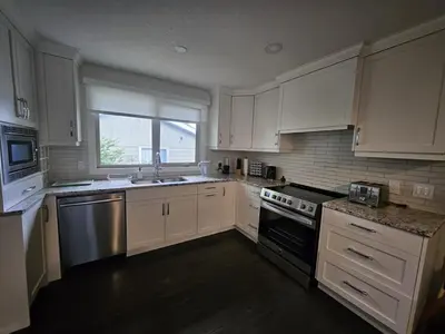 a kitchen with white cabinets and a sink and a stove at Luxurious Air Conditioned Inner City Bungalow in Calgary